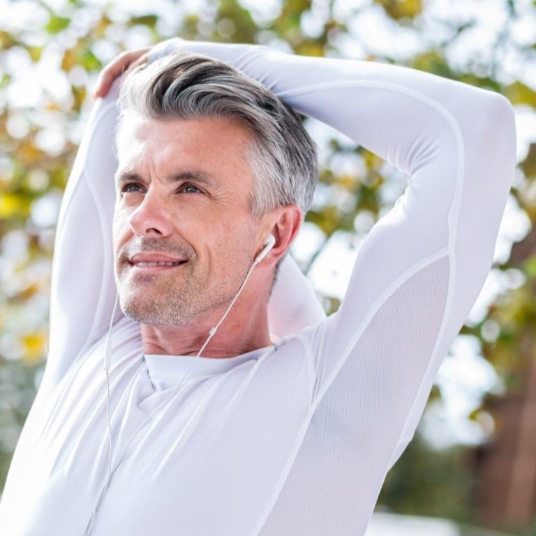 Website portrait- blog - How to 10x your health fit middle aged woman in athletic clothes pausing mid coastal run to bend forward and rest hands onto knees